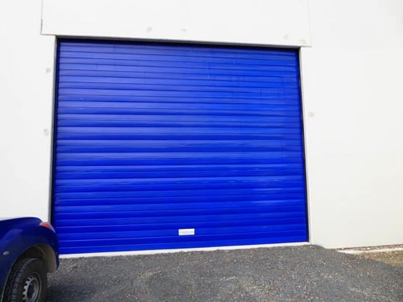 Blue industrial roller shutter door installed on a white warehouse exterior.